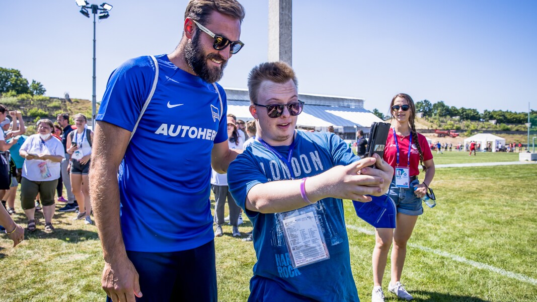 Auf dem Foto macht ein Athlet gerade ein Selfie gemeinsam mit einem Profi-Spieler von Hertha BSC.