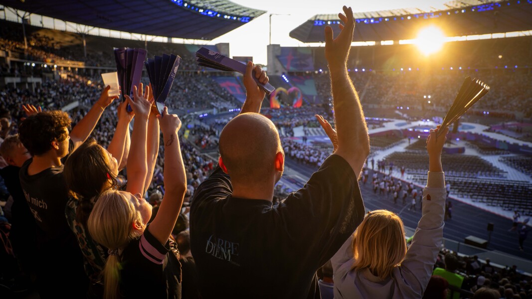 The photo shows cheering spectators at the opening ceremony in the Olympic Stadium. The mood is exuberant.