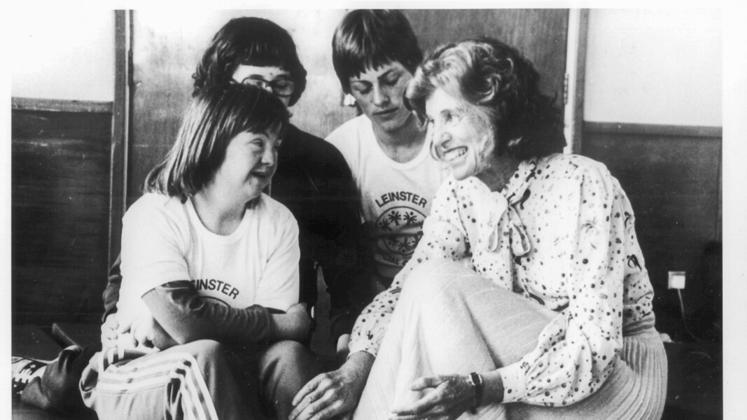 Das Bild zeigt Eunice Kennedy Shriver die mit Athleten auf einer Treppe sitzt und sich unterhält.
