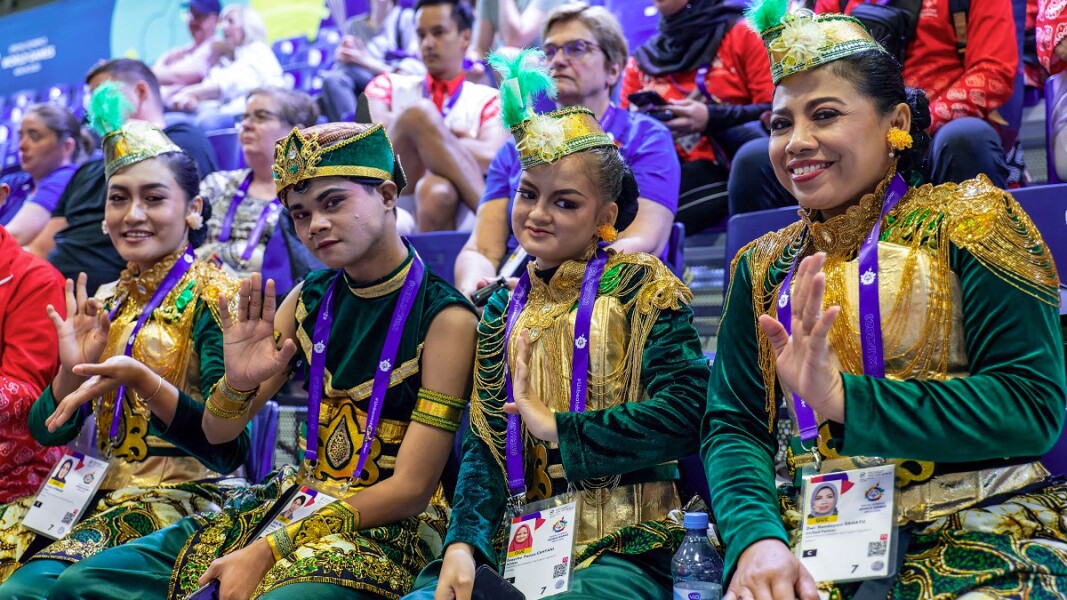 One male and three female gymnasts posing to the camera with a smile on their face with audience behind their back