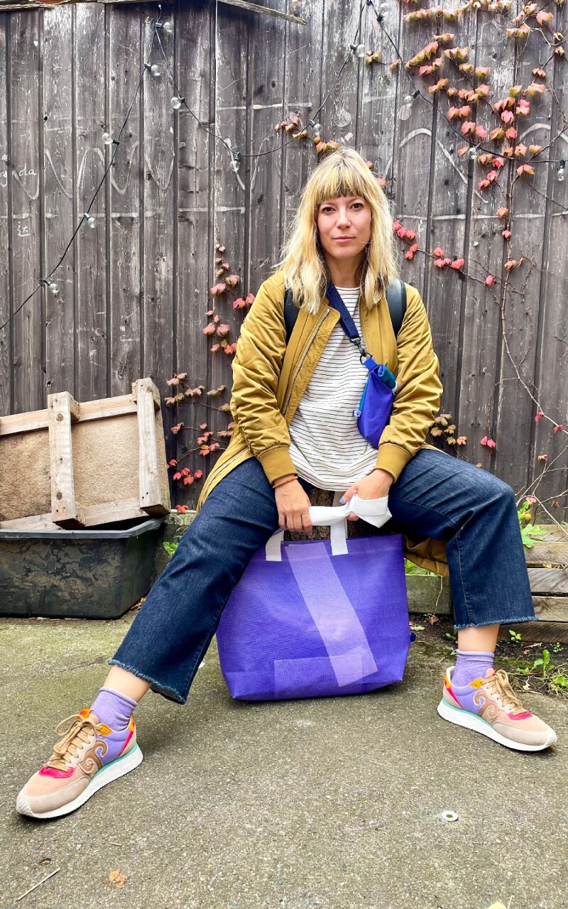 Auf dem Foto sitzt Mieze, die Frontsängerin der Band MiA., cool auf einer Holzbank. In ihren Händen hält sie eine upcycelte Tasche aus dem Special Olympics Shop.