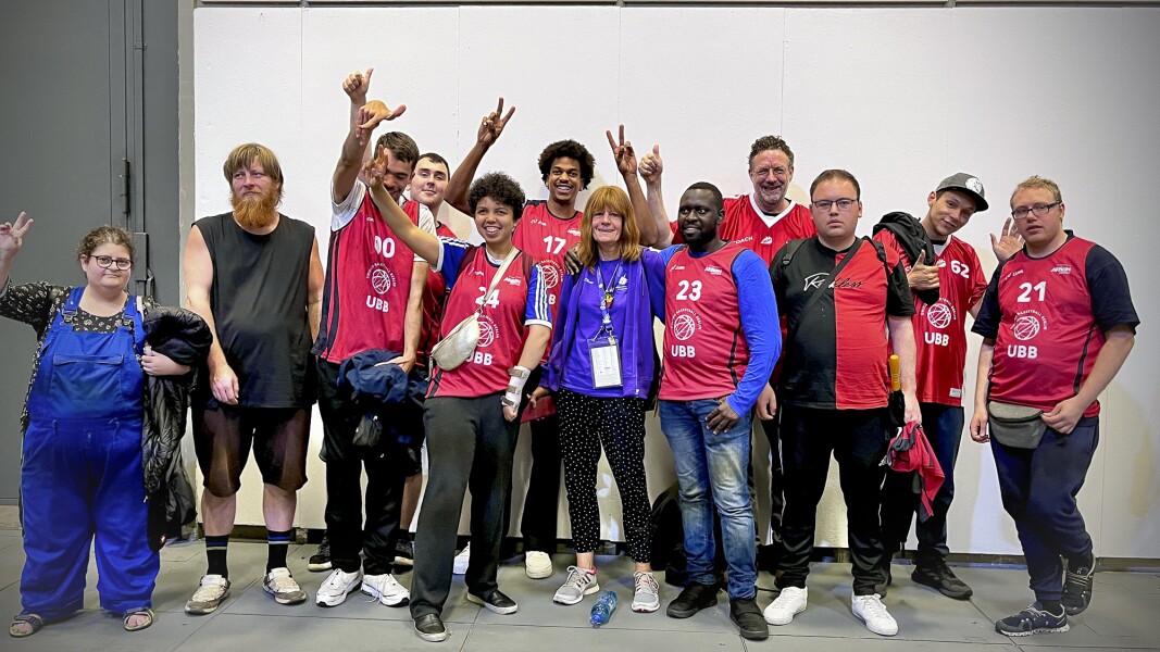 Eine Gruppe von Fans steht zusammen mit einer Volunteerin. Alle lächeln in die Kamera und winken.