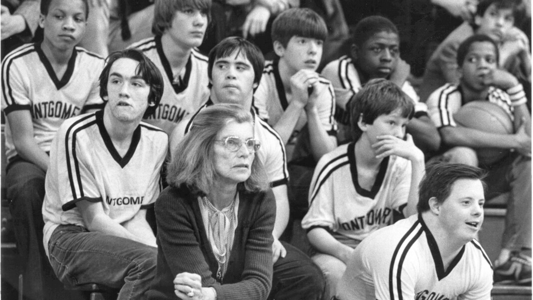 The photo shows Eunice Kennedy Shriver. She sits between athletes and follows a basketball game.