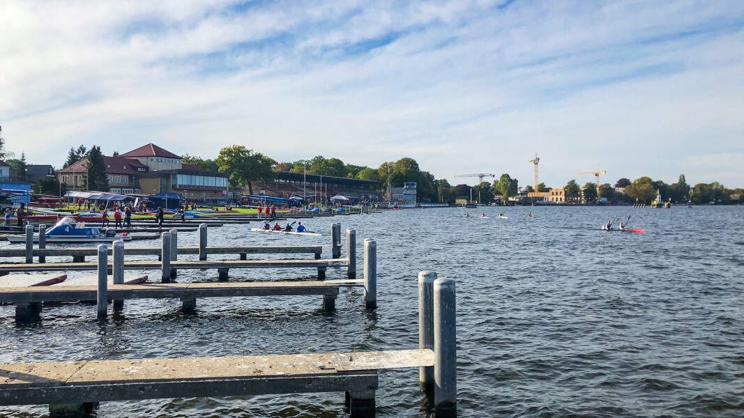 Das Foto zeigt die Regattastrecke in Grünau. Man sieht Kanus im Wasser und die Bootsanleger.