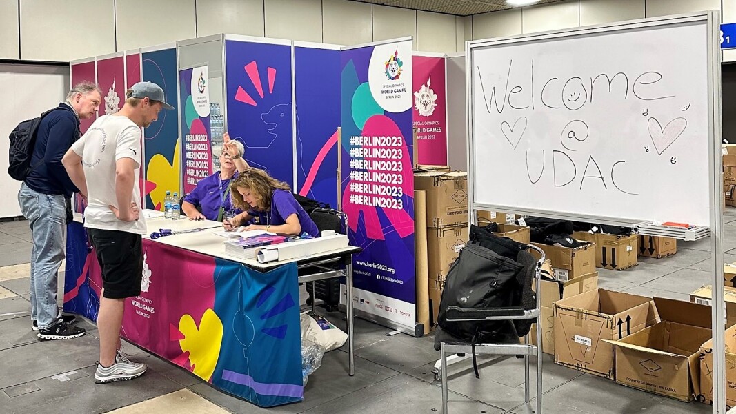 Das Foto zeigt den Eingang des UDAC, wo alle Volunteers herzlich begrüßt werden. An einem Info-Tisch sitzen zwei Team-Mitglieder und geben erste Informationen.