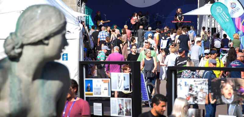 The photo shows a scene during the Special Olympics Festival 2022. Many people are crowding around the booths and in front of the stage where a band is performing. 