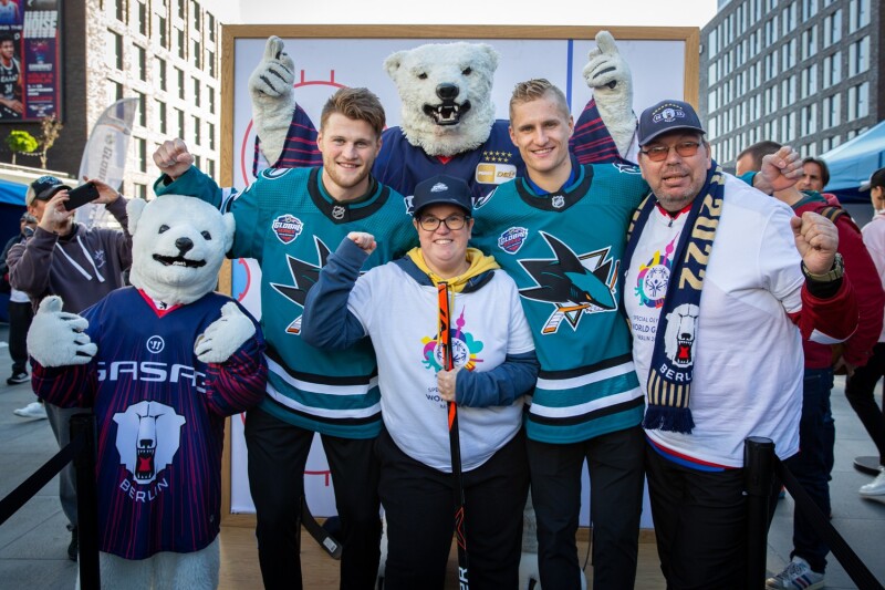 The photo shows the Eisbären Berlin mascot, two players and two representatives of Special Olympics. All cheer joyfully in the direction of the camera.