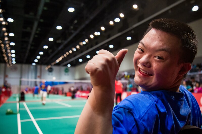 Auf dem Foto ist ein Athlet beim Badminton zu sehen, der lächelt und seinen Daumen nach oben zeigt.