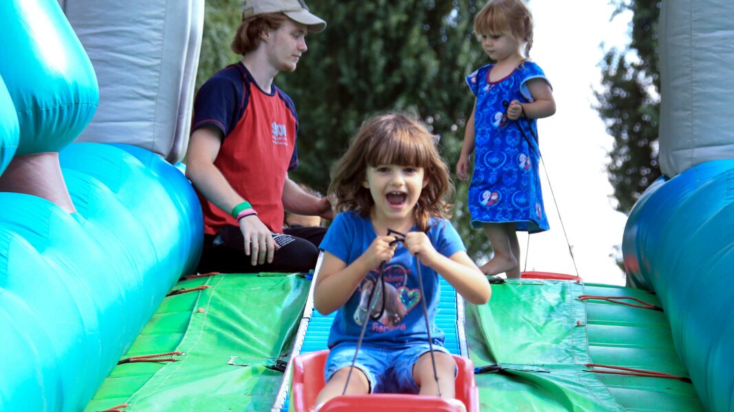 Das Foto zeigt ein junges kind, das im Rahmen des Familiensportfests Berlin mit einem Schlitten eine Rutsche runterrutscht. Es sieht dabei sehr fröhlich aus.