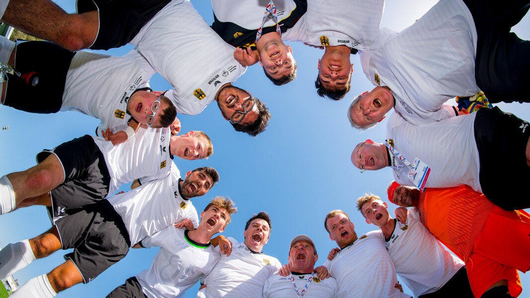 Auf dem Foto sieht man die Fußballmannschaft von Special Olympics Deutschland. Sie stehen im Kreis und rufen lautstark.
