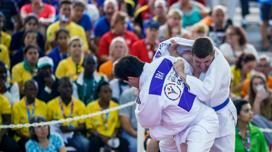 Auf dem Foto sind im Vordergrund zwei Judoka beim Kampf. Im Hintergrund sind volle Zuschauerränge zu sehen.