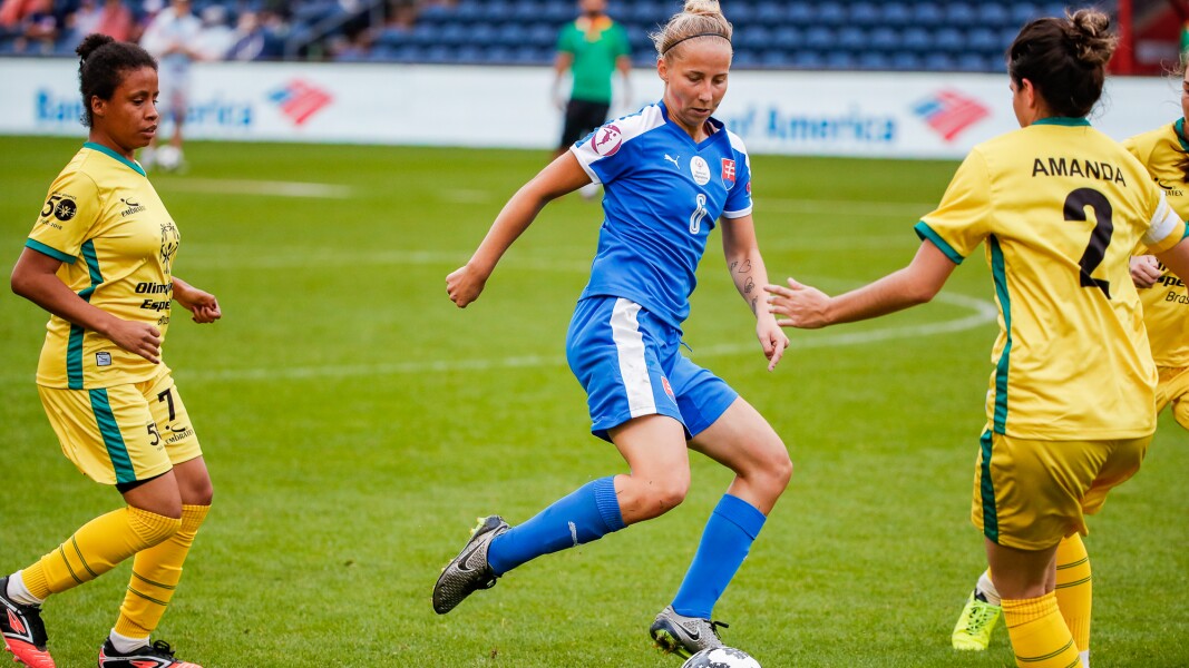 Das Foto zeigt drei Frauen die Fußball spielen. Sie sind konzentriert. Eine Spielerin passt den Ball.