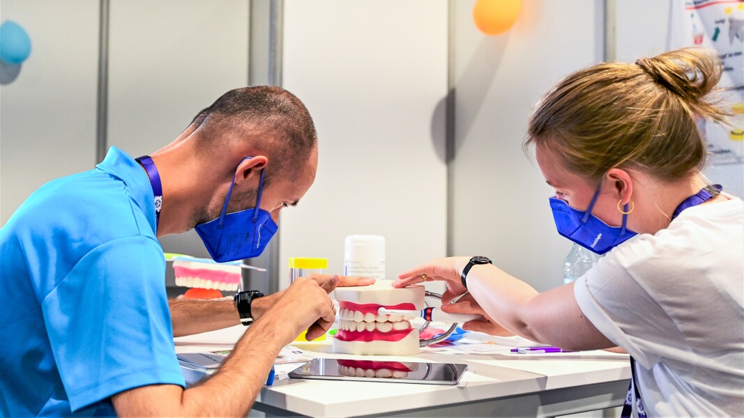 Das Foto zeigt eine Demonstration des richtigen Zähneputzens beim Healthy Athletes Programm "Special Smiles". Die Mitarbeiterin zeigt mit einer Zahnbürste an einem Modell-Gebiss wie der Athlet seine Zähne putzen sollte.