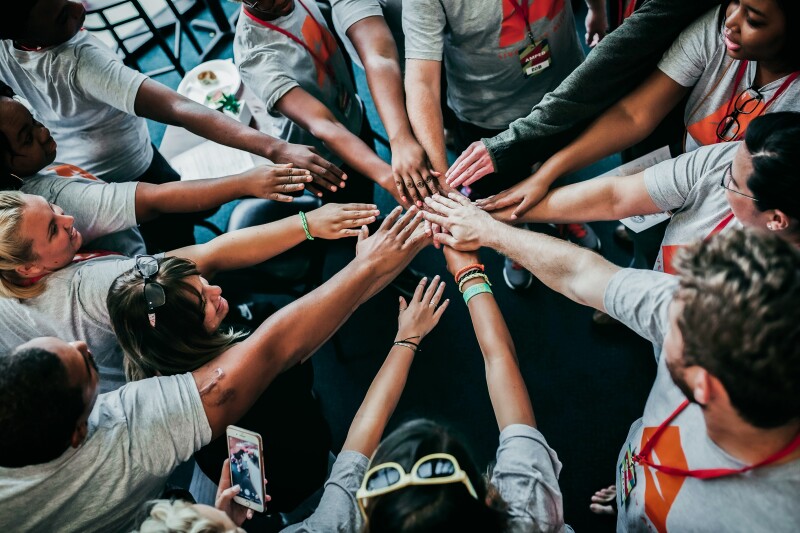 The photo shows a group of people standing in a circle. All of them hold their right arm in the middle to cheer.