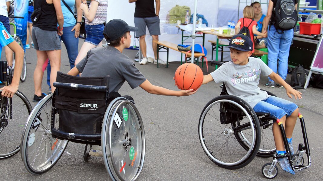 Das Foto zeigt zwei Kinder, die beide im Rollstuhl sitzen und Basketball spielen. Es ist im Rahmen des Familiensportfests Berlin aufgenommen worden.