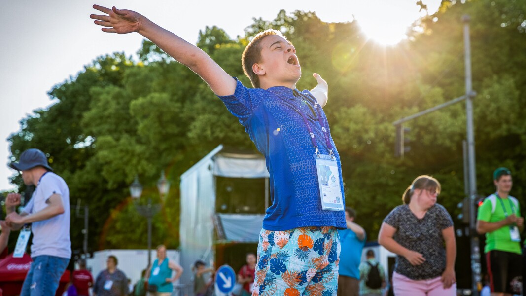 Auf dem Foto freut sich ein Athlet. Er hält beide Arme gestreckt hoch in die Luft, hat die Augen geschlossen und singt mit. Im Hintergrund sieht man weitere Feiernde.