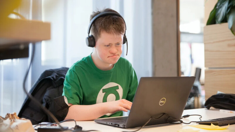 Das Bild zeigt Arthur Hackenthal an seinem Arbeitsplatz im lokalen Organisationskomitee der Weltspiele. Er trägt ein Headset und bedient gerade seinen Laptop.