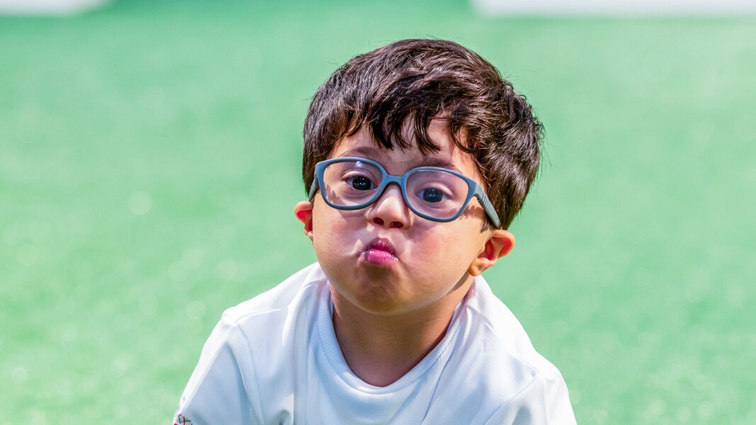 The photo shows a little boy with glasses. He forms a kissing mouth with his lips.