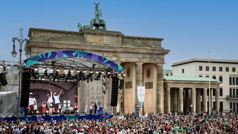 In the photo you can see the panorama of the athletes' disco at the Brandenburg Gate. In front of it is a big crowd and everyone is having fun and raising their arms.