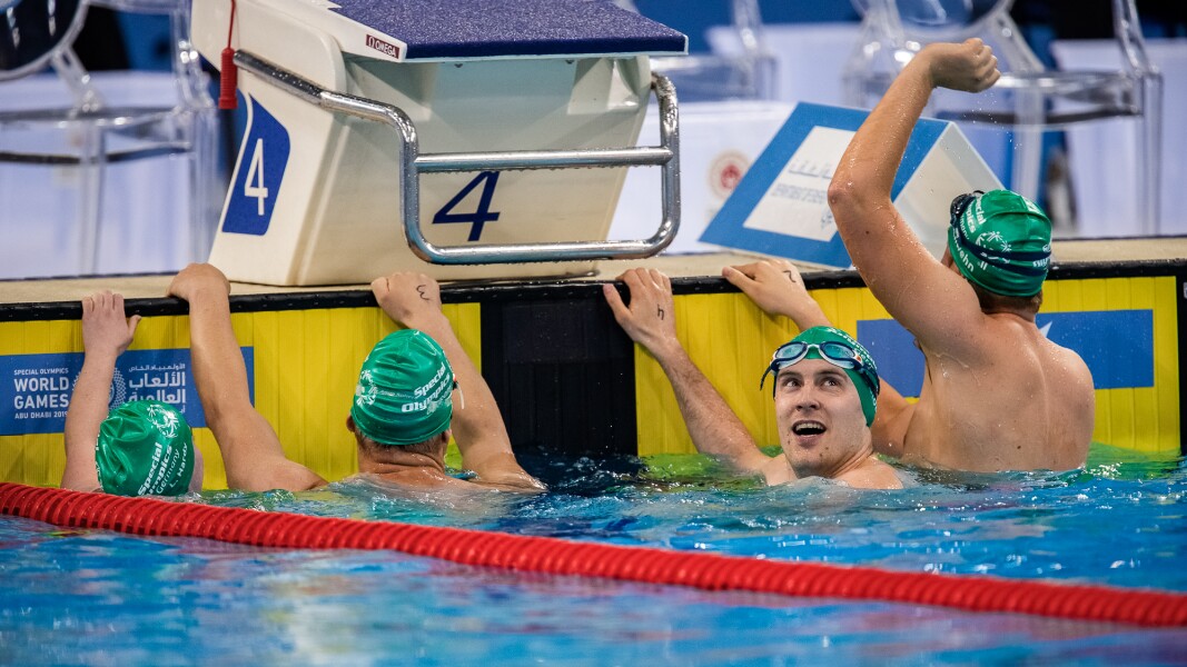 Das Foto zeigt vier Schwimmer nach dem Wettbewerb. Einer von ihnen reckt seinen Arm nach oben, ein anderer schaut auf die Zeitmessung.