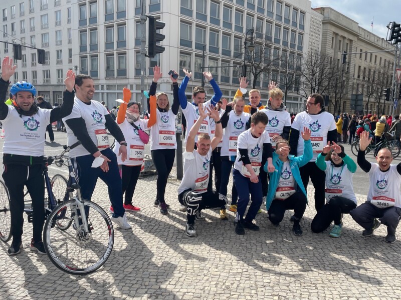 Das Foto zeigt eine Gruppe Special Olympics Athlet*innen und Betreuer*innen, die beim Berliner Halbmarathon am Start waren und gut gelaunt die Arme in die Höhe werfen.