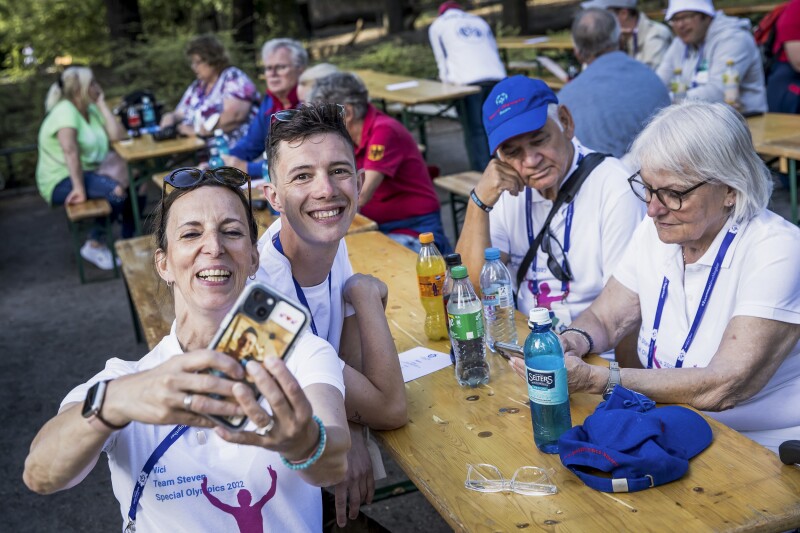 Das Foto zeigt eine Szene während des Familienempfangs der Nationalen Spiele. Vier Menschen sitzen an einem Tisch beisammen und eine Frau nimmt gerade ein Selfie von allen auf.