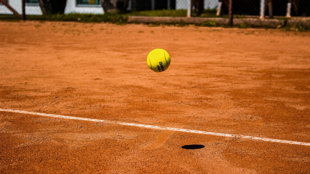 Auf dem Foto ist ein Tennisball auf einer roten Sandbahn zu sehen.
