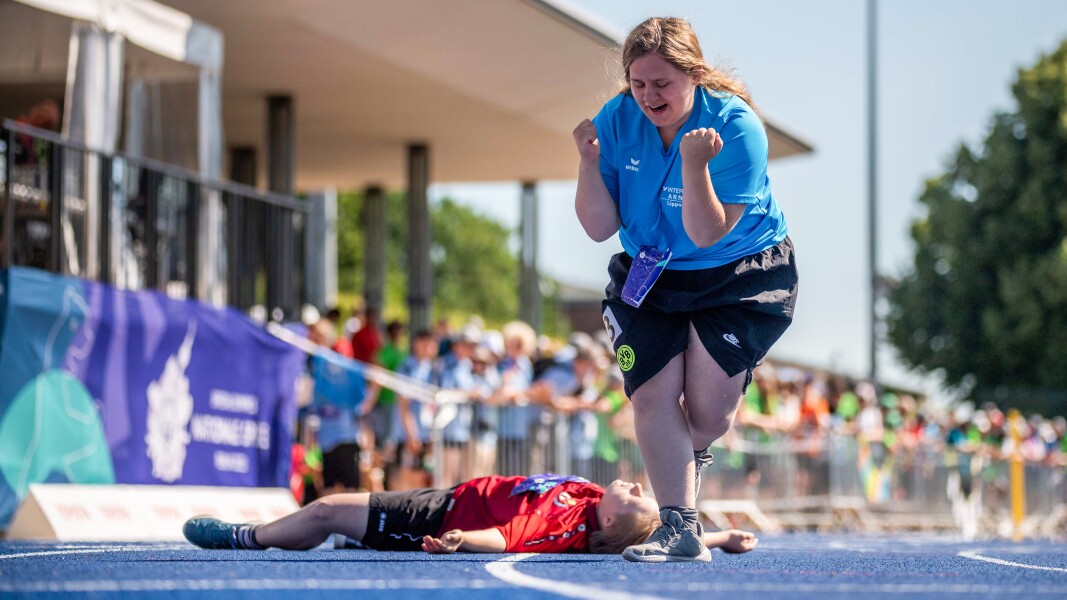 The photo shows the end of an athletics competition. One athlete is laying on the ground to take a breath and the second one is celebrating joyfully.