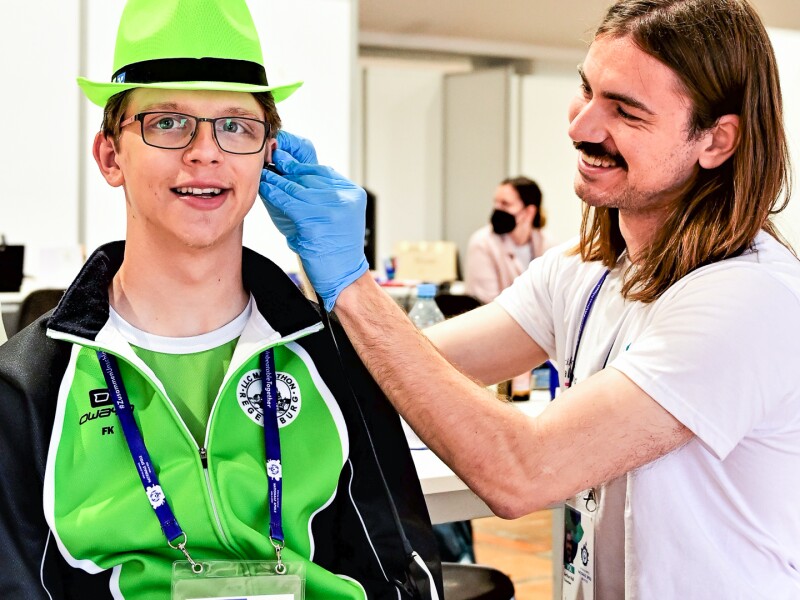 The photo shows a Healthy Hearing exam as part of the Healthy Athletes program. A doctor is examining the ear of an athlete who is smiling relaxedly at the camera.