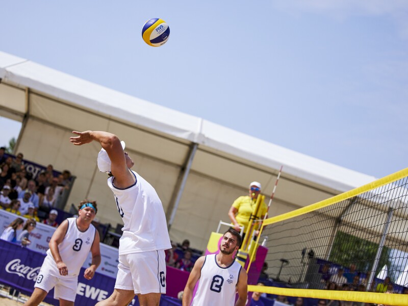 Ein Spieler der serbischen Beach Volleyball-Mannschaft holt nach hinten gebeugt zum Schlag über das Netz aus.