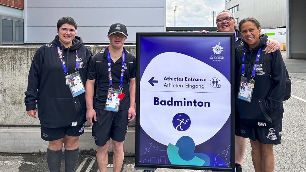 On the photo there are athletes in front of the badminton sign. They look happy