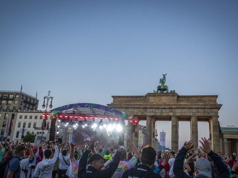The photo shows the Athletes' Party right in front of Brandenburg Gate. People are having fun with their arms raised in joy.