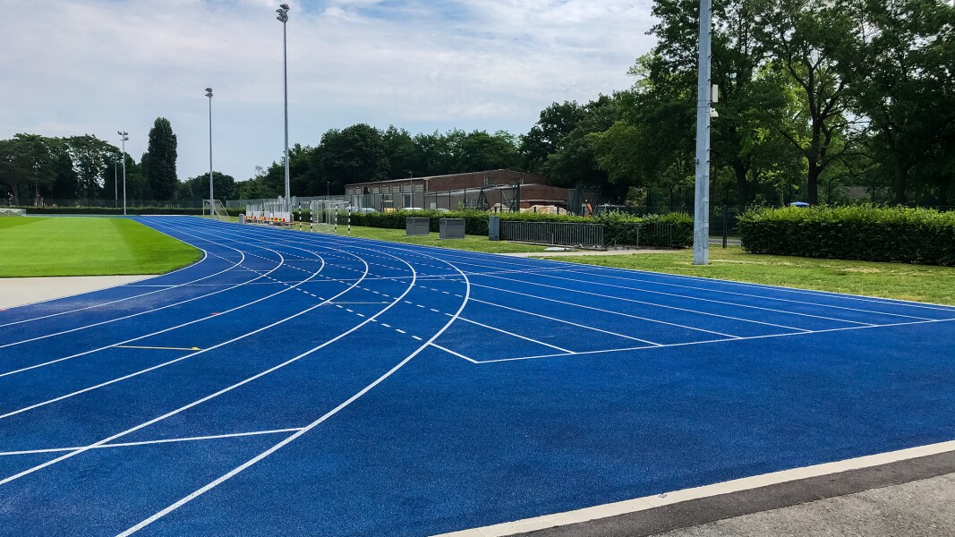 The photo shows a blue running track leading around a grassy area.