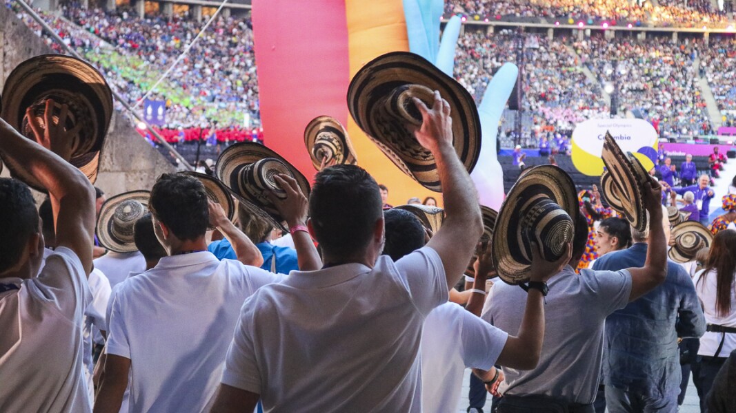 In the photo, athletes are running into a stadium. They raise their hats in greeting and are very happy.