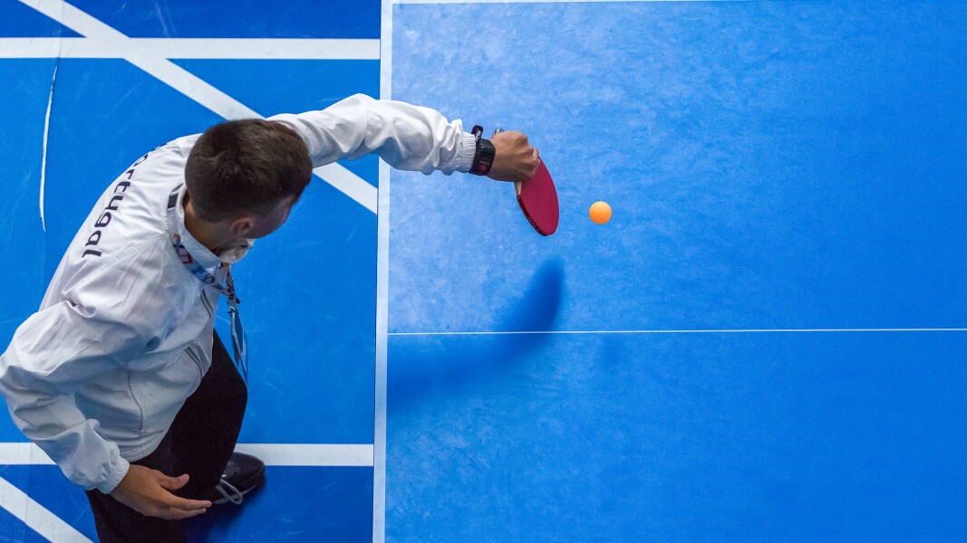 Das Foto zeigt einen Tischtennisspieler von oben. Er spielt gerade den Ball zurück.