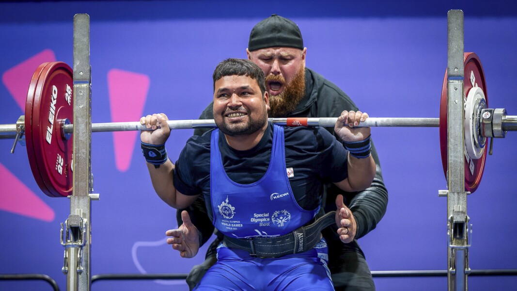 Das Foto zeigt eine Szene beim Kraftdreikampf. Der Athlet macht einen Squat und wird vom Sport Official angefeuert.