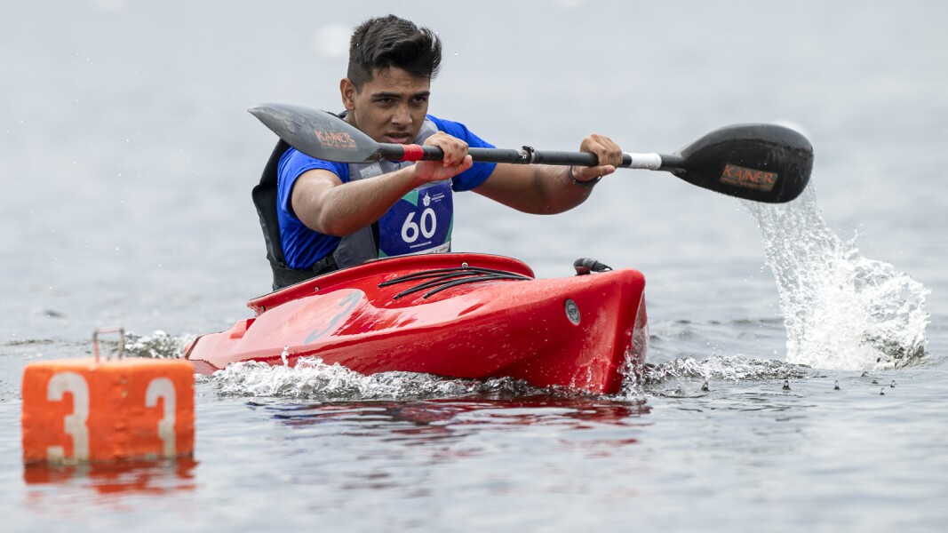 Ein Kanute in blauer Weste fährt ein rotes Kanu beim Wettkampf.