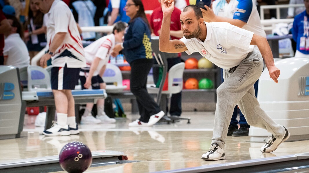Auf dem Foto ist ein Bowlingspieler während des Wettbewerbs zu sehen, der noch in der Wurfbewegung seiner Kugel ist.