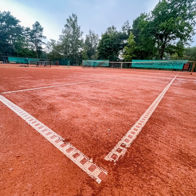 The photo shows a red outdoor tennis court. The focus is on one corner.