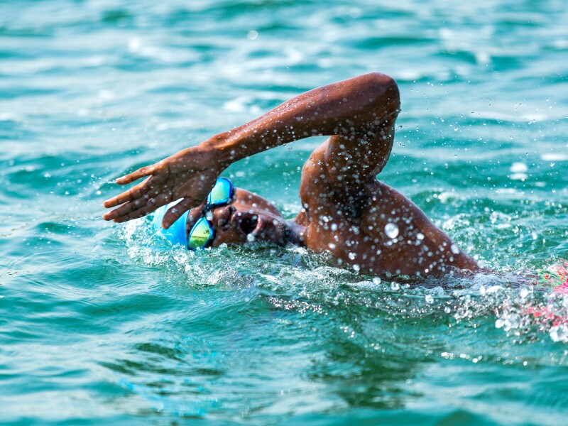Das Foto zeigt eine Athletin beim Freiwasserschwimmen. Wasser spritzt, während sie krault.