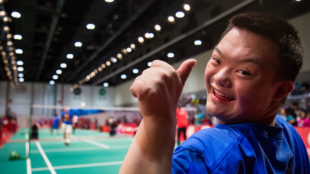 Auf dem Foto ist ein Athlet beim Badminton zu sehen, der lächelt und seinen Daumen nach oben zeigt.