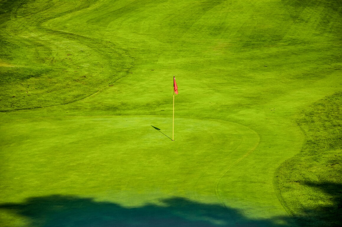 Das Foto zeigt einen Golfplatz mit leuchtend grünem rasen und einer roten Fahne beim Loch.