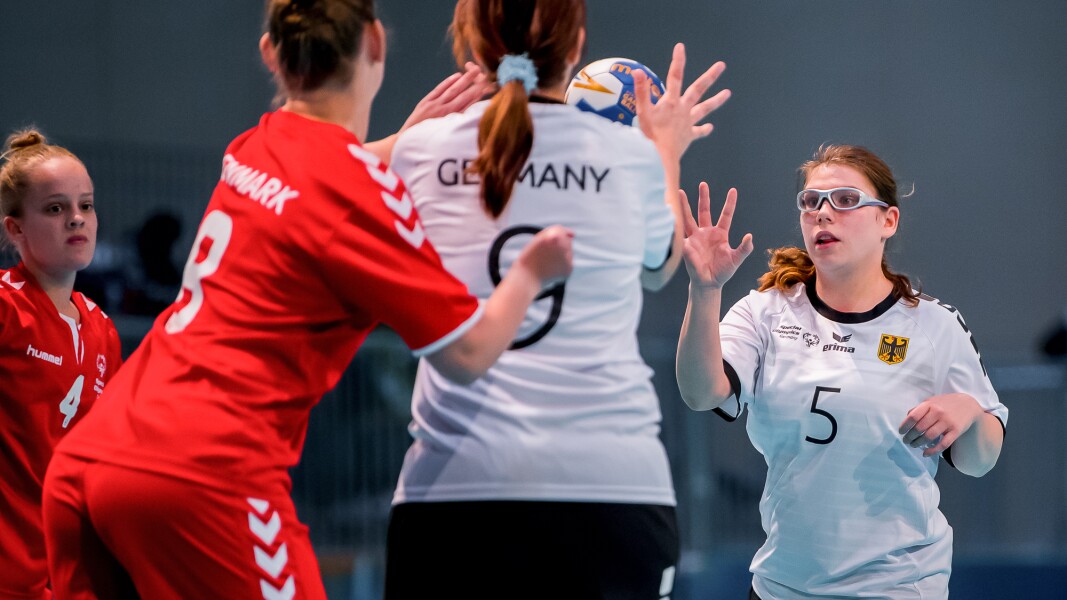 Das Foto zweigt vier Spielerinnen beim Handball. Eine Spielerin passt den Ball zu ihrer Mannschaftskollegin.