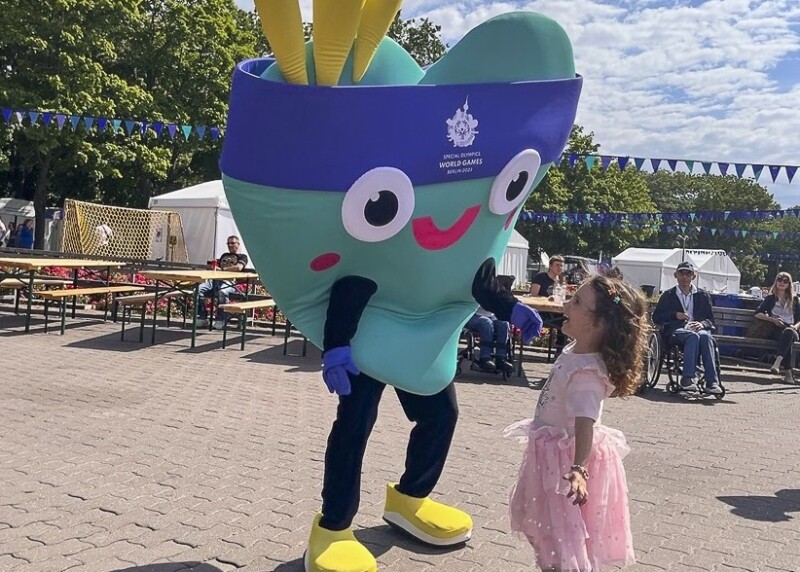 Auf dem Foto ist ein kleines Mädchen zu sehen. Sie lacht unser Maskottchen Unity an und freut sich riesig.