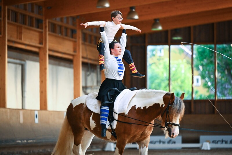 The photo shows a horse show during the World Games, when two vaulting athletes are doing a lifting figure on a horse.