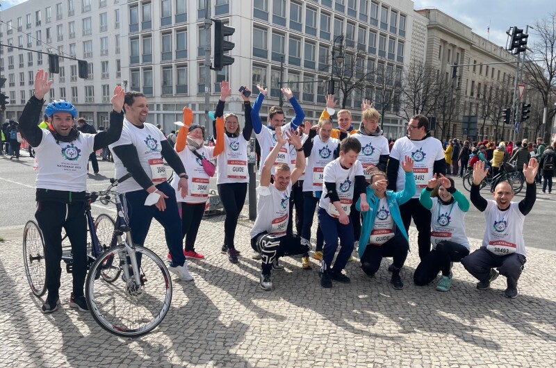 Das Foto zeigt eine Gruppe Special Olympics Athlet*innen und Betreuer*innen, die beim Berliner Halbmarathon am Start waren und gut gelaunt die Arme in die Höhe werfen.