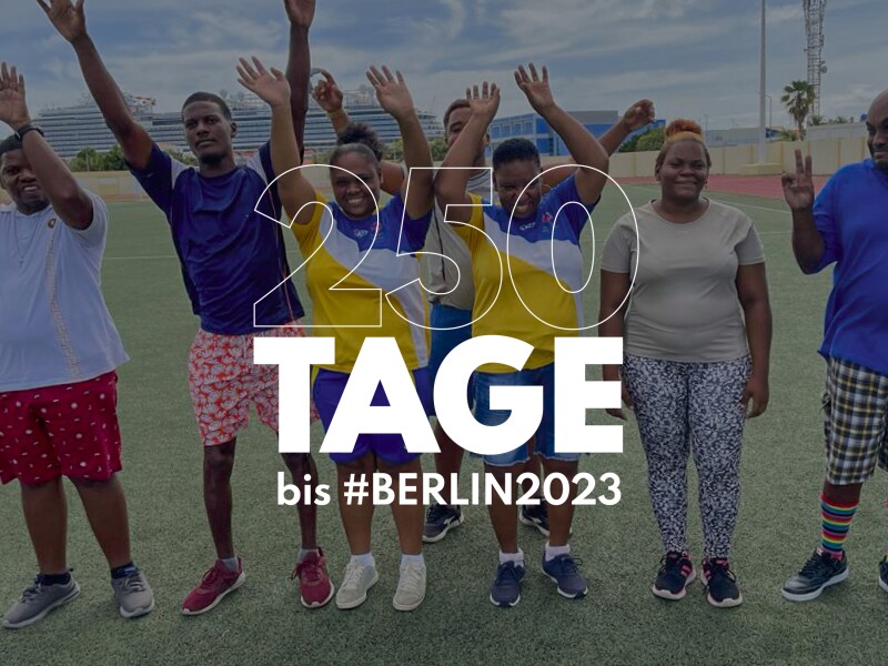 Auf der Grafik steht "250 Tage bis #Berlin2023". Im Hintergrund ist ein Foto von mehreren jubelnden Menschen zu sehen.