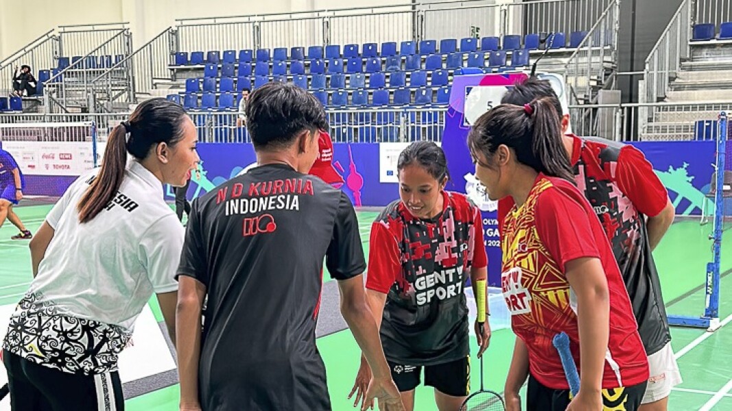 The photo shows athletes playing badminton. They join hands to cheer together.