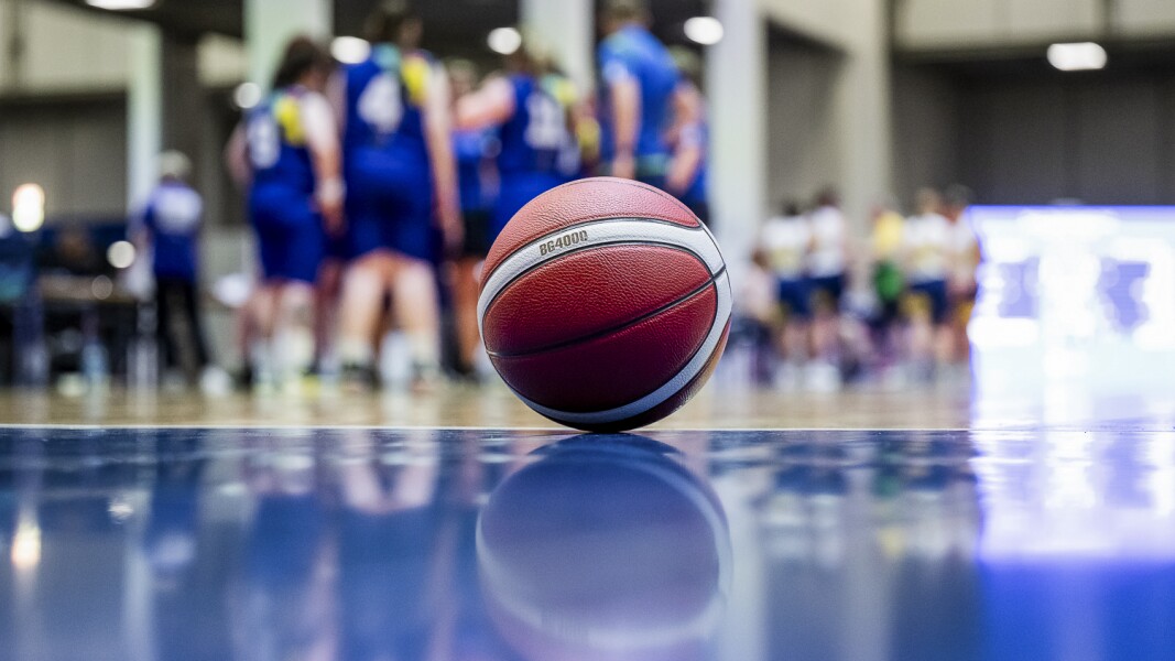 A basketball laying on the blue court with players in the background