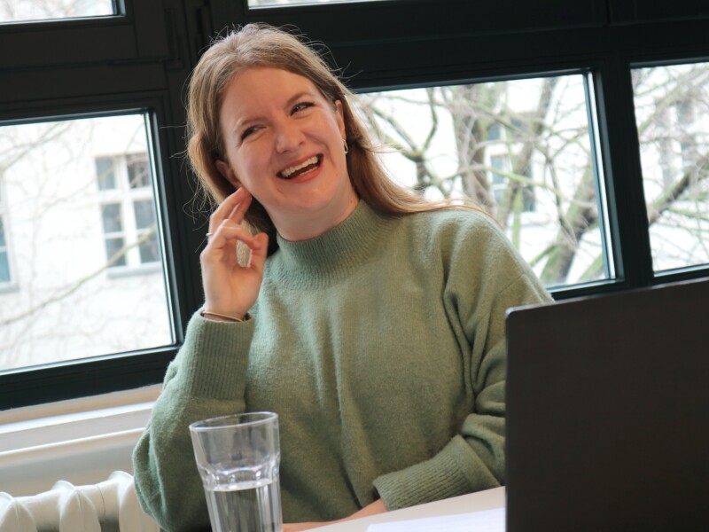 The photo shows our employee Georgia Royes during the interview on the topic "Fans in the Stands". She laughs happily and looks in the direction of the interview partner.